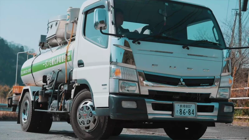 道路を走る白いバキュームカー。車体と運転席が見える。