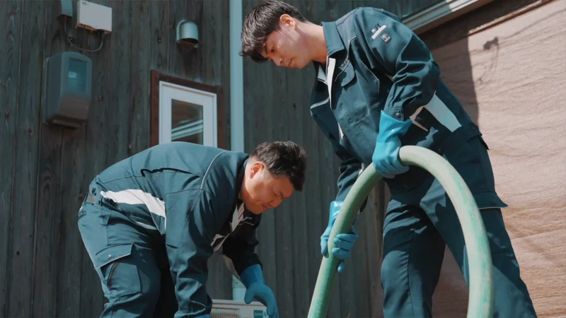 建物の前で、二人のスタッフがホースを扱っている。