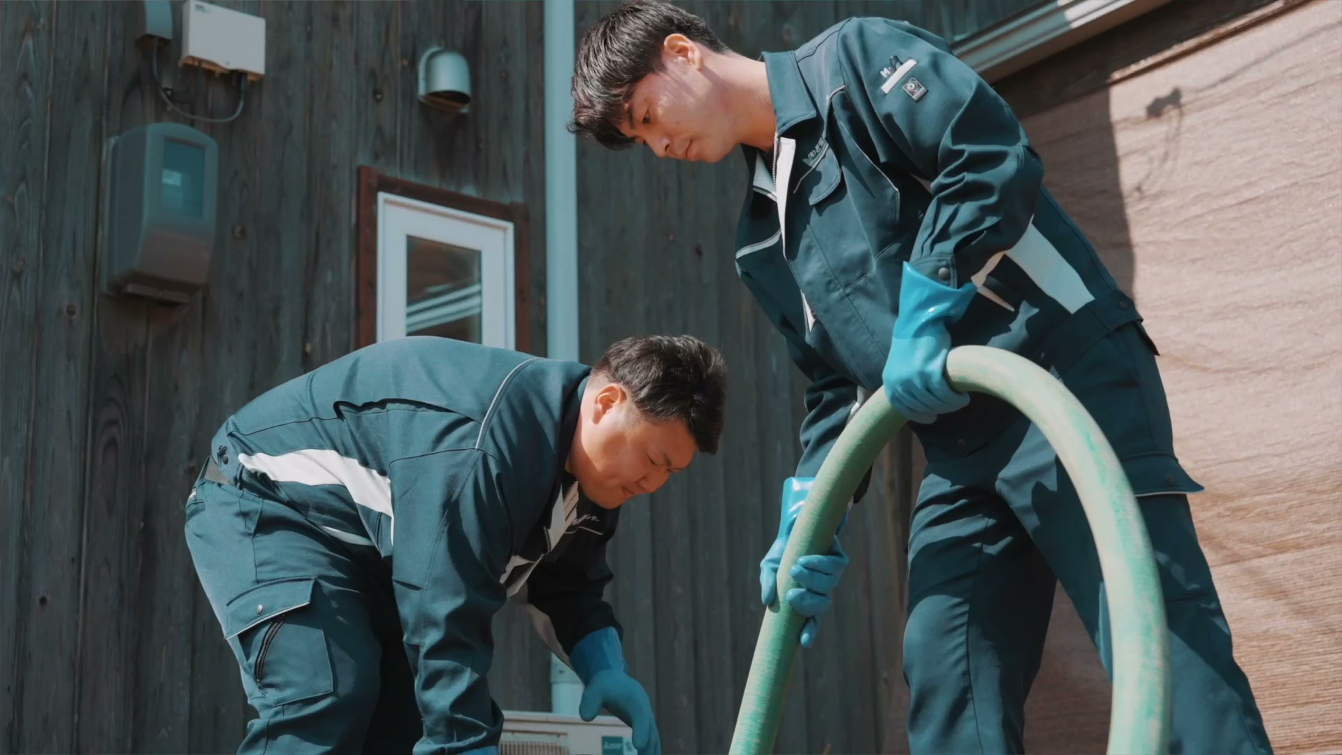 建物の前で、2人のスタッフがホースを扱う仕事風景